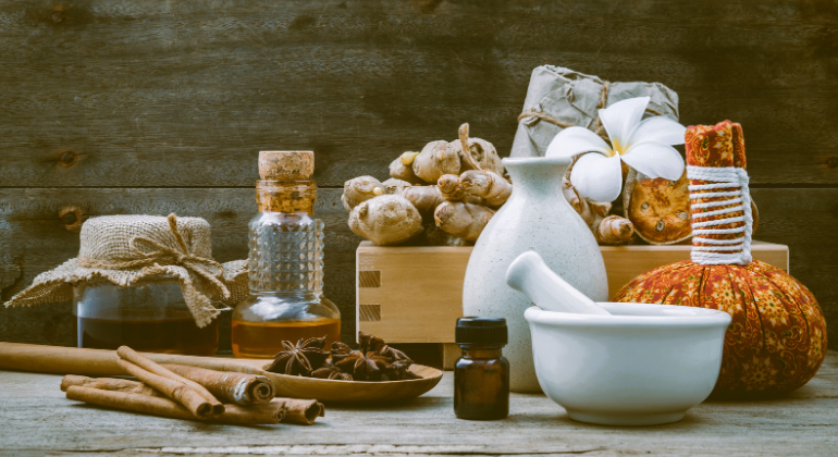 A collection of Ayurvedic herbs, oils, spices, and traditional healing tools arranged on a wooden surface, representing natural remedies and holistic wellness.