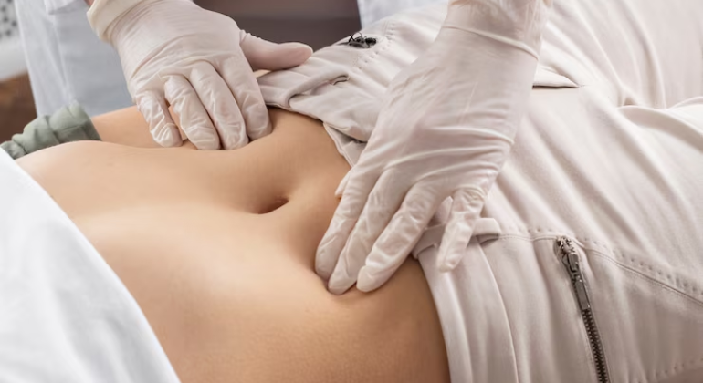 A healthcare professional wearing gloves examining a patient's abdomen, pressing near the navel area, possibly checking for navel displacement or digestive issues.