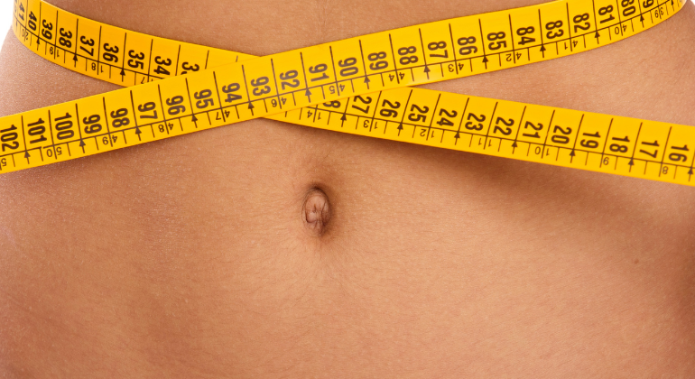 Close-up of a person’s abdomen with yellow measuring tape wrapped around the waist, symbolizing concerns related to navel position, abdominal alignment, or waist measurement in manual therapy.